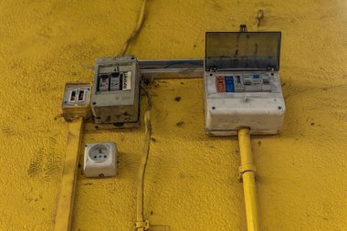Kirli sarı bir duvardaki hasarlı elektrik prizi, hasarlı elektrik tesisatı, elektrik hırsızlığı, yasadışı 220V kurulumu