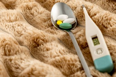 Bir termometre hasta bir hastanın yüksek ateşini, grip salgınını, soğuk algınlığı ilaçlarını, elektronik termometreyi ve yataktaki battaniyenin üzerindeki hapları gösteriyor.