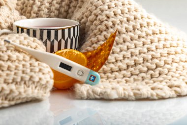 Masaya serilmiş grip ve soğuk algınlığı ilaçları, sıcaklığı ölçmek için bir termometre, ısınan çay, fincana sarılmış bir eşarp, grip salgını.,