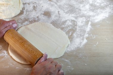 Hamuru elle yoğurmak ve mutfak tezgahında ahşap bir oklavayla yuvarlamak, mantarlı mantar ve etli geleneksel hamur işi, Noel tarifleri.