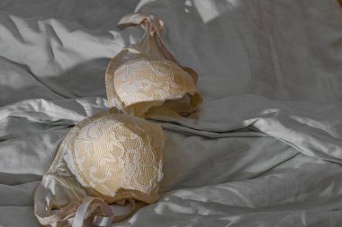 Bir otel odasındaki çarşaflara saçılmış kadın kıyafetleri, çarşafların üzerinde bir sütyen, otel kangurusunda aşıkların buluşması.