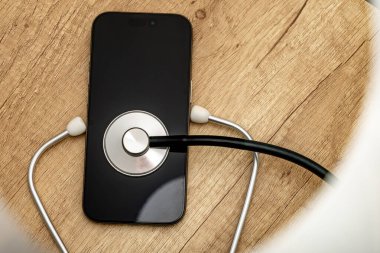 Siyah ekranlı hasarlı bir cep telefonu ahşap servis masasına yerleştiriliyor, steteskop kulaklıklarıyla, telefonu kendin tamir etmeye çalışırken, cep telefonu servisi...