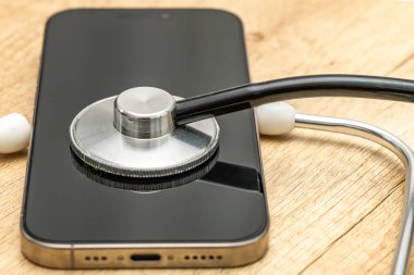 Siyah ekranlı hasarlı bir cep telefonu ahşap servis masasına yerleştiriliyor, steteskop kulaklıklarıyla, telefonu kendin tamir etmeye çalışırken, cep telefonu servisi...