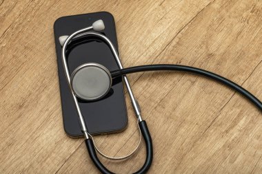 Siyah ekranlı hasarlı bir cep telefonu ahşap servis masasına yerleştiriliyor, steteskop kulaklıklarıyla, telefonu kendin tamir etmeye çalışırken, cep telefonu servisi...