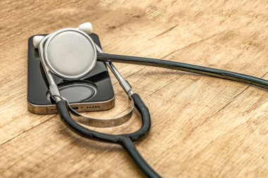 Siyah ekranlı hasarlı bir cep telefonu ahşap servis masasına yerleştiriliyor, steteskop kulaklıklarıyla, telefonu kendin tamir etmeye çalışırken, cep telefonu servisi...