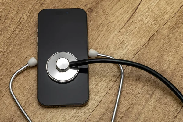 Siyah ekranlı hasarlı bir cep telefonu ahşap servis masasına yerleştiriliyor, steteskop kulaklıklarıyla, telefonu kendin tamir etmeye çalışırken, cep telefonu servisi...