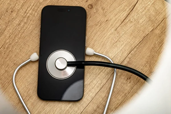 Siyah ekranlı hasarlı bir cep telefonu ahşap servis masasına yerleştiriliyor, steteskop kulaklıklarıyla, telefonu kendin tamir etmeye çalışırken, cep telefonu servisi...