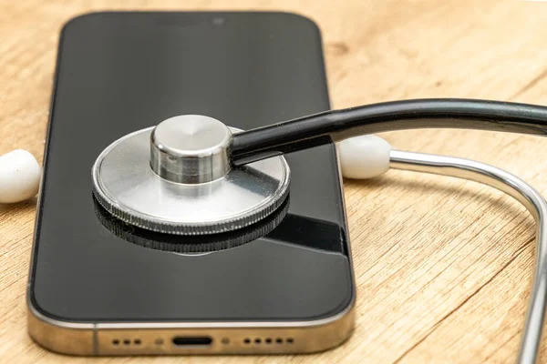 Siyah ekranlı hasarlı bir cep telefonu ahşap servis masasına yerleştiriliyor, steteskop kulaklıklarıyla, telefonu kendin tamir etmeye çalışırken, cep telefonu servisi...