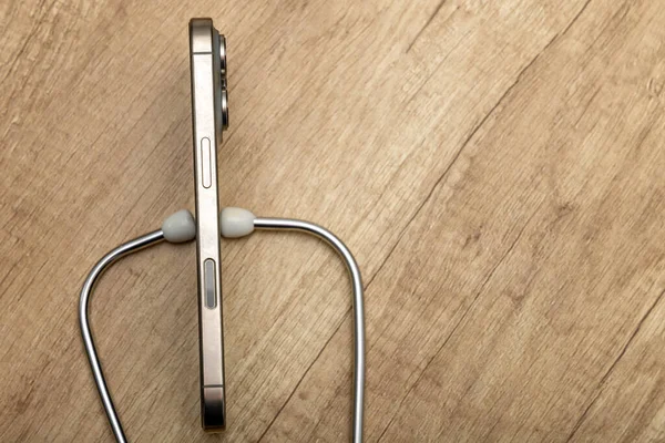 Hasarlı bir cep telefonu ahşap servis masasına yerleştirilmiş, steteskop kulaklıkları, telefon arızası aramak, telefonu kendin tamir etmeye çalışmak, cep telefonu servisi.