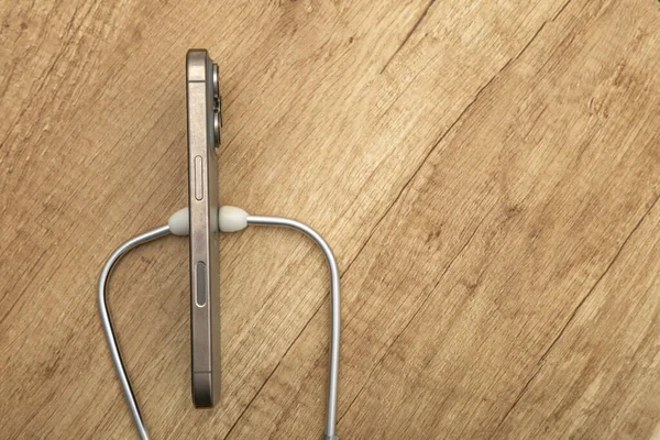 Hasarlı bir cep telefonu ahşap servis masasına yerleştirilmiş, steteskop kulaklıkları, telefon arızası aramak, telefonu kendin tamir etmeye çalışmak, cep telefonu servisi.