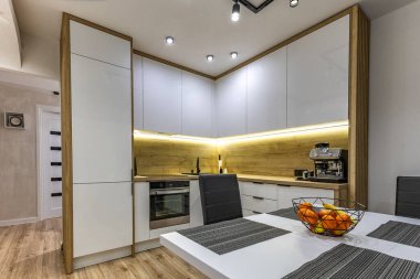 Modern mutfak mobilyaları, beyaz parlak ön kaplamalı mobilyalar, mutfaklı modern oturma odası, apartman yenilenmesi, fırınlı fonksiyonel mutfak mobilyası, indüksiyon hob, kahve makinesi, mutfakta siyah lavabo.