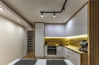 Modern mutfak mobilyaları, beyaz parlak ön kaplamalı mobilyalar, mutfaklı modern oturma odası, apartman yenilenmesi, fırınlı fonksiyonel mutfak mobilyası, indüksiyon hob, kahve makinesi, mutfakta siyah lavabo.