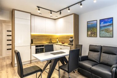 Modern mutfak mobilyaları, beyaz parlak ön kaplamalı mobilyalar, mutfaklı modern oturma odası, apartman yenilenmesi, fırınlı fonksiyonel mutfak mobilyası, indüksiyon hob, kahve makinesi, mutfakta siyah lavabo.