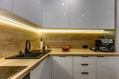 Modern mutfak mobilyaları, beyaz parlak ön kaplamalı mobilyalar, mutfaklı modern oturma odası, apartman yenilenmesi, fırınlı fonksiyonel mutfak mobilyası, indüksiyon hob, kahve makinesi, mutfaktaki siyah lavabo.