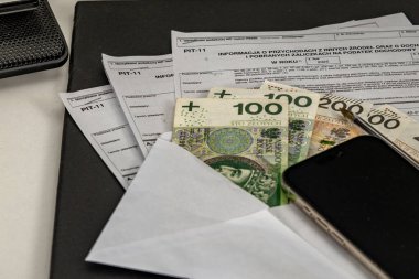 Masada tamamlanmış bir PIT-11 vergi iade formu gelir vergisi, cep telefonu ve muhasebe bürosundaki bir masanın üzerindeki banknotlar için para.,