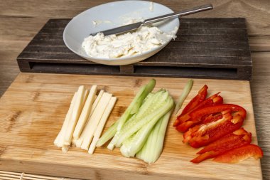 Geleneksel Japon tarifine göre suşi malzemeleri mutfaktaki ahşap tezgaha yerleştirilmiş kırmızı biber, sarı peynir, yeşil salatalık, bıçakla suşi malzemesi kesme, taze suşi hazırlama.