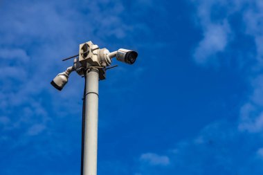 Mavi gökyüzüne karşı uzun bir direğe monte edilmiş bir sokak güvenlik kamerası, halka açık yerlerde kayıt yapmak yasak, belediye servisleri tarafından video izleme yasak