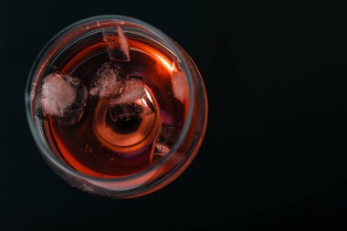 Siyah bir zemin üzerinde kırmızı şarap bulunan dar bir bardak, bir şarap kadehinin içine buz düşmüş, alkolsüz bir şarap kadehine dökülmüş.