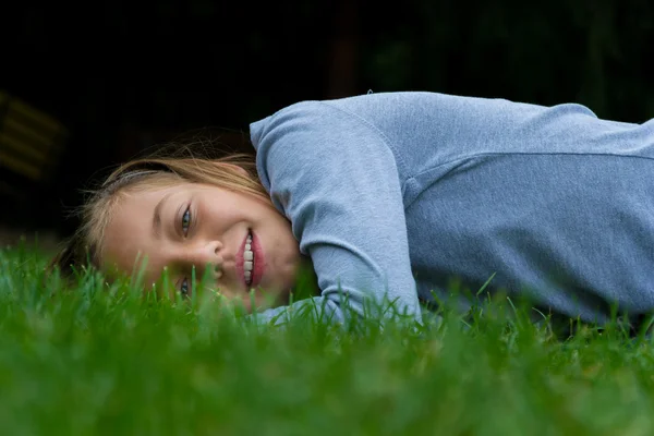 Unga barn flicka lägger åt sidan i gräs ler med öppen mun — Stockfoto