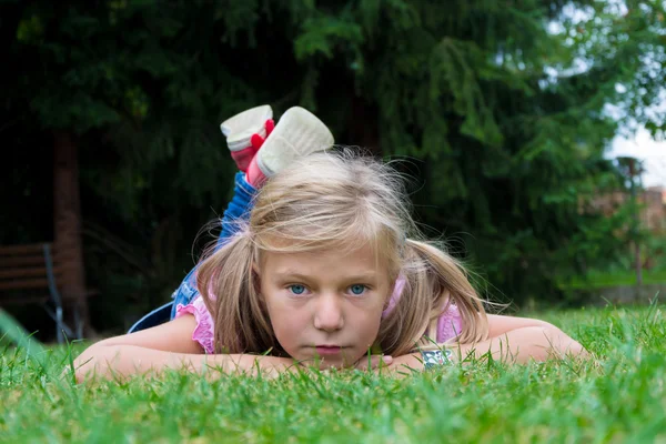 Liten blond flicka med hästsvans låg i gräset njuter summ — Stockfoto