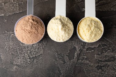 Protein powder. A spoonful of protein powder on a table. Different flavors of whey protein powder. Sports nutrition concept. Gym. Amino acid food supplement, creatine powder. Copy space.