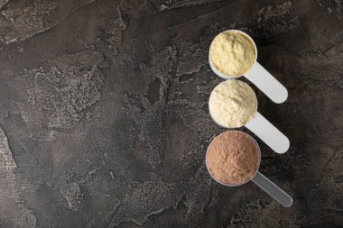 Protein powder. A spoonful of protein powder on a table. Different flavors of whey protein powder. Sports nutrition concept. Gym. Amino acid food supplement, creatine powder. Copy space.