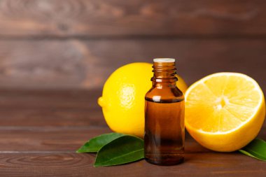 Limon dilimlenmiş limonlu bir şişede limon yağı ve ahşap bir arka planda yapraklar. Limon yağı. Aromatik esanslı parfüm şişesi. Serum, limon özü. C vitamini. Doğal kozmetik ürünler. Aromaterapi. Spa mı? Metin için boşluk.