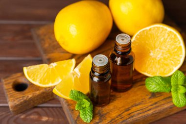 Limon dilimlenmiş limonlu bir şişede limon yağı ve ahşap bir arka planda yapraklar. Limon yağı. Aromatik esanslı parfüm şişesi. Serum, limon özü. C vitamini. Doğal kozmetik ürünler. Aromaterapi. Spa mı? Metin için boşluk.