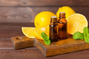 Limon dilimlenmiş limonlu bir şişede limon yağı ve ahşap bir arka planda yapraklar. Limon yağı. Aromatik esanslı parfüm şişesi. Serum, limon özü. C vitamini. Doğal kozmetik ürünler. Aromaterapi. Spa mı? Metin için boşluk.