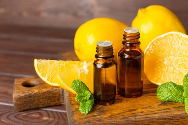 Limon dilimlenmiş limonlu bir şişede limon yağı ve ahşap bir arka planda yapraklar. Limon yağı. Aromatik esanslı parfüm şişesi. Serum, limon özü. C vitamini. Doğal kozmetik ürünler. Aromaterapi. Spa mı? Metin için boşluk.