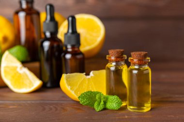 Limon dilimlenmiş limonlu bir şişede limon yağı ve ahşap bir arka planda yapraklar. Limon yağı. Aromatik esanslı parfüm şişesi. Serum, limon özü. C vitamini. Doğal kozmetik ürünler. Aromaterapi. Spa mı? Metin için boşluk.