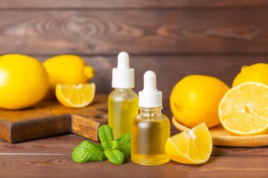 Limon dilimlenmiş limonlu bir şişede limon yağı ve ahşap bir arka planda yapraklar. Limon yağı. Aromatik esanslı parfüm şişesi. Serum, limon özü. C vitamini. Doğal kozmetik ürünler. Aromaterapi. Spa mı? Metin için boşluk.