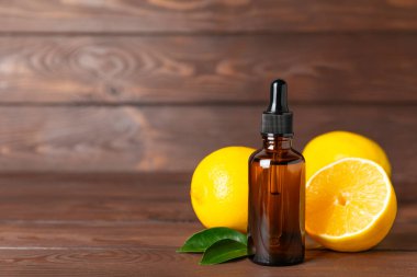 Limon dilimlenmiş limonlu bir şişede limon yağı ve ahşap bir arka planda yapraklar. Limon yağı. Aromatik esanslı parfüm şişesi. Serum, limon özü. C vitamini. Doğal kozmetik ürünler. Aromaterapi. Spa mı? Metin için boşluk.