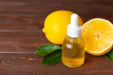 Limon dilimlenmiş limonlu bir şişede limon yağı ve ahşap bir arka planda yapraklar. Limon yağı. Aromatik esanslı parfüm şişesi. Serum, limon özü. C vitamini. Doğal kozmetik ürünler. Aromaterapi. Spa mı? Metin için boşluk.