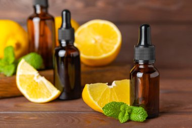 Limon dilimlenmiş limonlu bir şişede limon yağı ve ahşap bir arka planda yapraklar. Limon yağı. Aromatik esanslı parfüm şişesi. Serum, limon özü. C vitamini. Doğal kozmetik ürünler. Aromaterapi. Spa mı? Metin için boşluk.