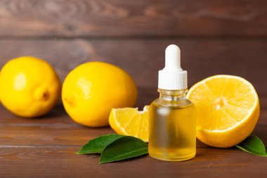 Limon dilimlenmiş limonlu bir şişede limon yağı ve ahşap bir arka planda yapraklar. Limon yağı. Aromatik esanslı parfüm şişesi. Serum, limon özü. C vitamini. Doğal kozmetik ürünler. Aromaterapi. Spa mı? Metin için boşluk.