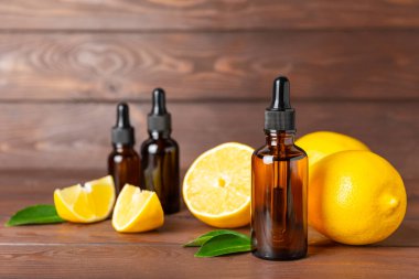 Limon dilimlenmiş limonlu bir şişede limon yağı ve ahşap bir arka planda yapraklar. Limon yağı. Aromatik esanslı parfüm şişesi. Serum, limon özü. C vitamini. Doğal kozmetik ürünler. Aromaterapi. Spa mı? Metin için boşluk.
