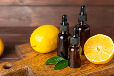 Limon dilimlenmiş limonlu bir şişede limon yağı ve ahşap bir arka planda yapraklar. Limon yağı. Aromatik esanslı parfüm şişesi. Serum, limon özü. C vitamini. Doğal kozmetik ürünler. Aromaterapi. Spa mı? Metin için boşluk.