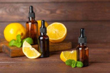 Limon dilimlenmiş limonlu bir şişede limon yağı ve ahşap bir arka planda yapraklar. Limon yağı. Aromatik esanslı parfüm şişesi. Serum, limon özü. C vitamini. Doğal kozmetik ürünler. Aromaterapi. Spa mı? Metin için boşluk.