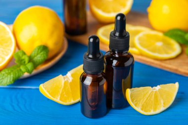 Limon dilimlenmiş limonlu bir şişede limon yağı ve ahşap bir arka planda yapraklar. Limon yağı. Aromatik esanslı parfüm şişesi. Serum, limon özü. C vitamini. Doğal kozmetik ürünler. Aromaterapi. Spa mı? Metin için boşluk.