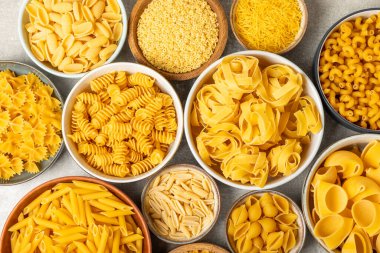 Arka plandaki kaselerde pişmemiş İtalyan makarnası çeşitleri. Kuru makarna çeşitleri, üst manzara, yemek arka planı. Farklı türde pişmemiş makarna. Malzemeler. Fırında pişmemiş İtalyan makarnası.