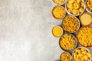 Arka plandaki kaselerde pişmemiş İtalyan makarnası çeşitleri. Kuru makarna çeşitleri, üst manzara, yemek arka planı. Farklı türde pişmemiş makarna. Malzemeler. Fırında pişmemiş İtalyan makarnası.