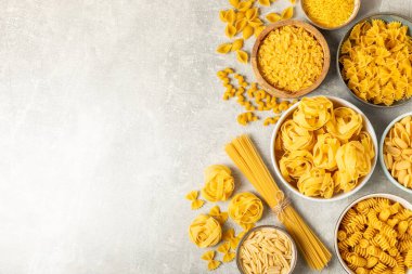 Arka plandaki kaselerde pişmemiş İtalyan makarnası çeşitleri. Kuru makarna çeşitleri, üst manzara, yemek arka planı. Farklı türde pişmemiş makarna. Malzemeler. Fırında pişmemiş İtalyan makarnası.