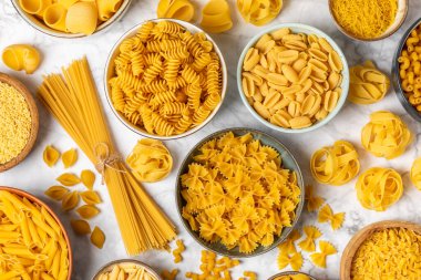 Arka plandaki kaselerde pişmemiş İtalyan makarnası çeşitleri. Kuru makarna çeşitleri, üst manzara, yemek arka planı. Farklı türde pişmemiş makarna. Malzemeler. Fırında pişmemiş İtalyan makarnası.