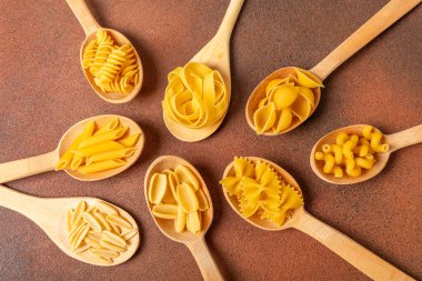 Arka plandaki kaselerde pişmemiş İtalyan makarnası çeşitleri. Kuru makarna çeşitleri, üst manzara, yemek arka planı. Farklı türde pişmemiş makarna. Malzemeler. Fırında pişmemiş İtalyan makarnası.