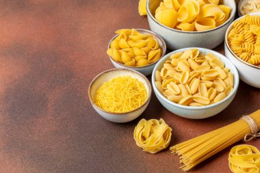 Arka plandaki kaselerde pişmemiş İtalyan makarnası çeşitleri. Kuru makarna çeşitleri, üst manzara, yemek arka planı. Farklı türde pişmemiş makarna. Malzemeler. Fırında pişmemiş İtalyan makarnası.