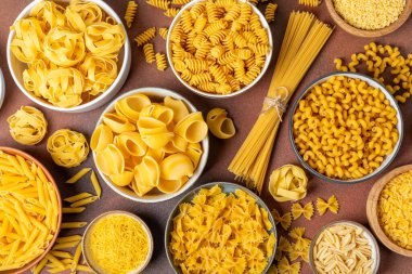 Arka plandaki kaselerde pişmemiş İtalyan makarnası çeşitleri. Kuru makarna çeşitleri, üst manzara, yemek arka planı. Farklı türde pişmemiş makarna. Malzemeler. Fırında pişmemiş İtalyan makarnası.