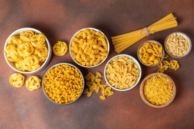 Arka plandaki kaselerde pişmemiş İtalyan makarnası çeşitleri. Kuru makarna çeşitleri, üst manzara, yemek arka planı. Farklı türde pişmemiş makarna. Malzemeler. Fırında pişmemiş İtalyan makarnası.