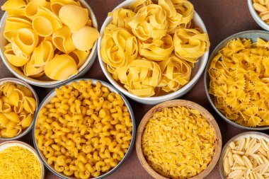 Kavanozda pişmemiş makarna. Arka planda çeşitli İtalyan kuru makarna şekilleri, üst görünüm. Yemek geçmişi. Makarna çeşitleri. çiğ makarna