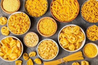 Kavanozda pişmemiş makarna. Arka planda çeşitli İtalyan kuru makarna şekilleri, üst görünüm. Yemek geçmişi. Makarna çeşitleri. çiğ makarna